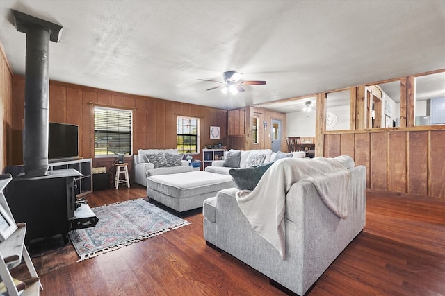 living room with a wood stove, dark wood-type flooring, wooden walls, ceiling fan, and a textured ceiling