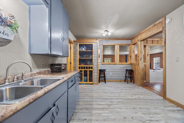 kitchen featuring sink, blue cabinets, wood walls, a textured ceiling, and light wood-type flooring