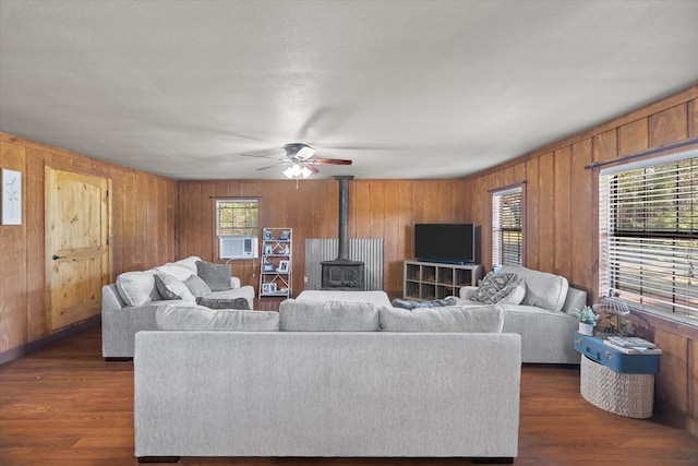 living room with dark hardwood / wood-style flooring, a textured ceiling, ceiling fan, wooden walls, and a wood stove