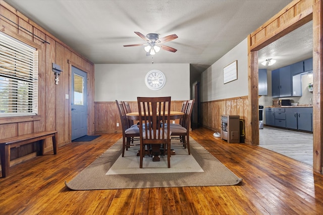 dining space featuring a textured ceiling, ceiling fan, wooden walls, and dark hardwood / wood-style floors