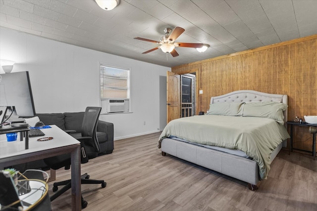 bedroom featuring ceiling fan, cooling unit, light wood-type flooring, wooden walls, and ornamental molding