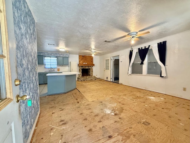 kitchen with sink, ceiling fan, a textured ceiling, a stone fireplace, and white fridge
