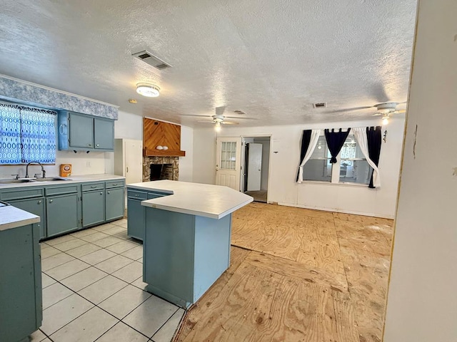 kitchen featuring sink, ceiling fan, a center island, a fireplace, and a textured ceiling