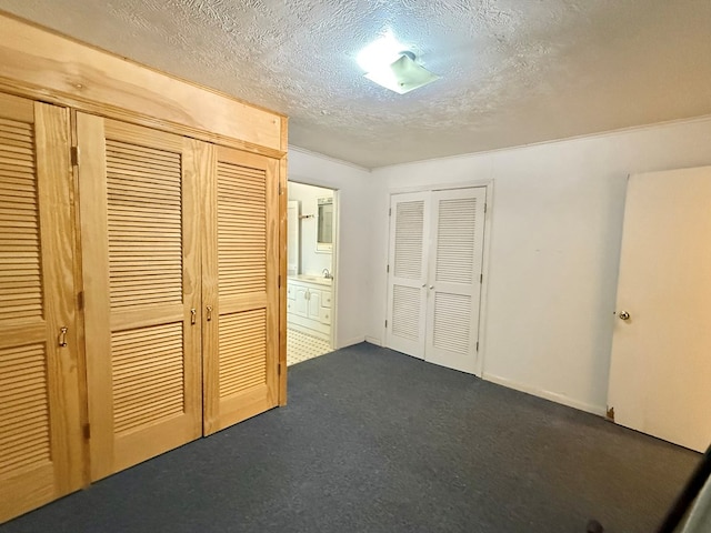 unfurnished bedroom featuring dark carpet, a textured ceiling, and ensuite bathroom