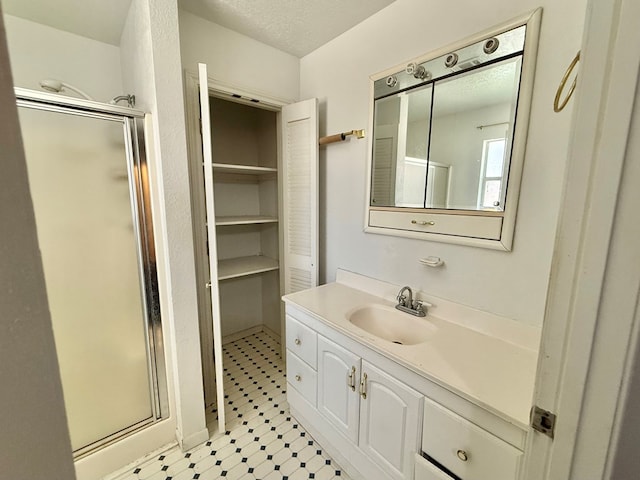 bathroom with a shower with door, vanity, and a textured ceiling