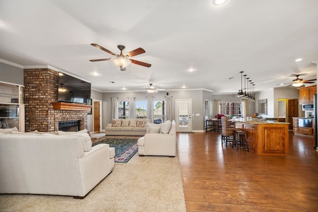 living area featuring a ceiling fan, a brick fireplace, crown molding, and recessed lighting
