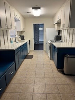 kitchen featuring sink, blue cabinets, white cabinetry, gas range oven, and light tile patterned flooring