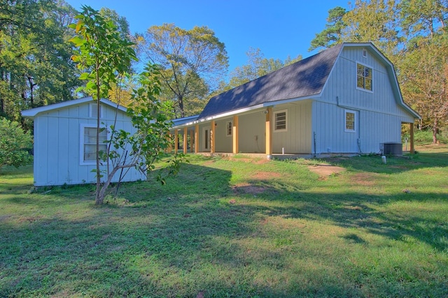 exterior space featuring an outbuilding, roof with shingles, a lawn, a gambrel roof, and cooling unit