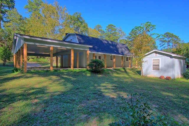 back of property featuring an outbuilding, roof with shingles, a carport, and a lawn