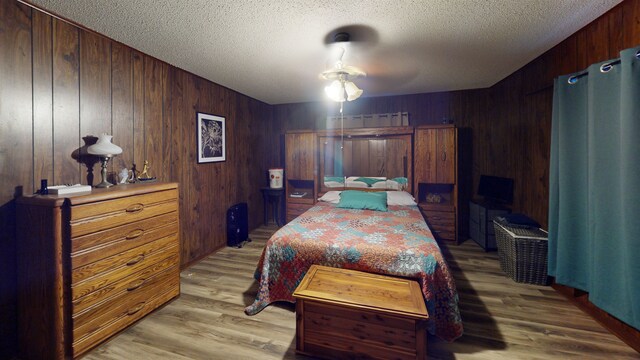 bedroom with ceiling fan, wood walls, a textured ceiling, and light hardwood / wood-style flooring