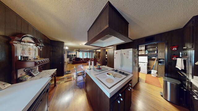 kitchen featuring light wood-type flooring, custom range hood, a textured ceiling, white appliances, and wooden walls