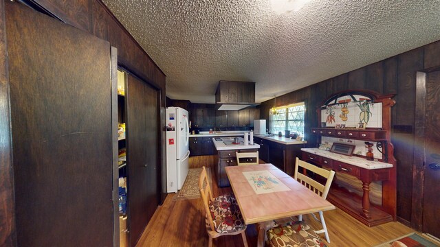 kitchen featuring wooden walls, white fridge, light hardwood / wood-style floors, and a textured ceiling