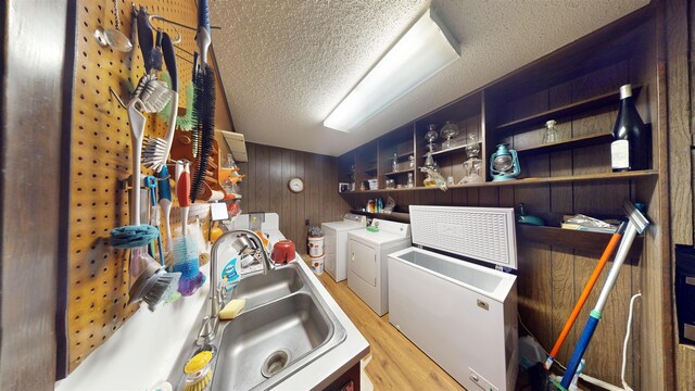 interior space featuring a textured ceiling, wooden walls, sink, light hardwood / wood-style flooring, and washing machine and clothes dryer