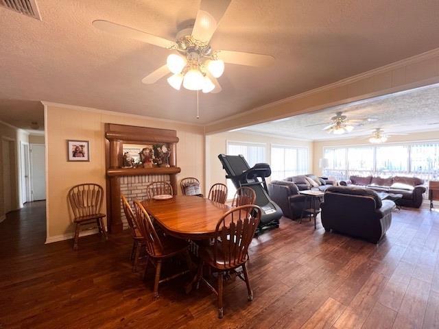 dining area with a brick fireplace, ceiling fan, ornamental molding, a textured ceiling, and dark hardwood / wood-style flooring