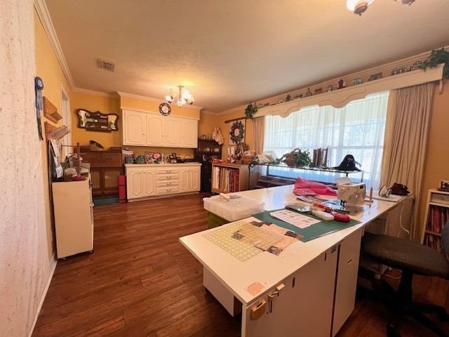 kitchen with white cabinetry, dark wood-type flooring, a kitchen breakfast bar, a notable chandelier, and ornamental molding