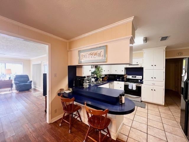 kitchen featuring range with electric cooktop, light hardwood / wood-style floors, a textured ceiling, white cabinets, and ornamental molding