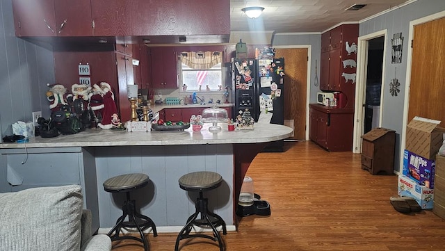 kitchen featuring a breakfast bar, ornamental molding, kitchen peninsula, and black fridge with ice dispenser