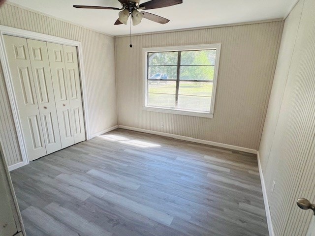 unfurnished bedroom featuring ceiling fan, ornamental molding, a closet, and light hardwood / wood-style flooring