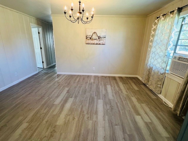 unfurnished dining area featuring wood-type flooring, crown molding, cooling unit, and an inviting chandelier