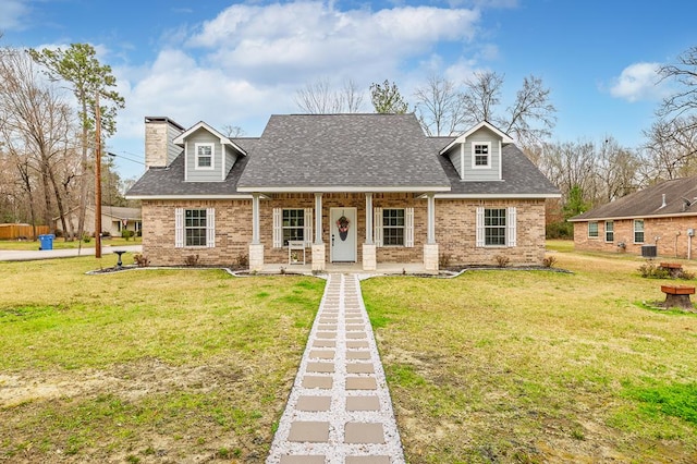 cape cod house featuring brick siding, a chimney, roof with shingles, a porch, and a front yard