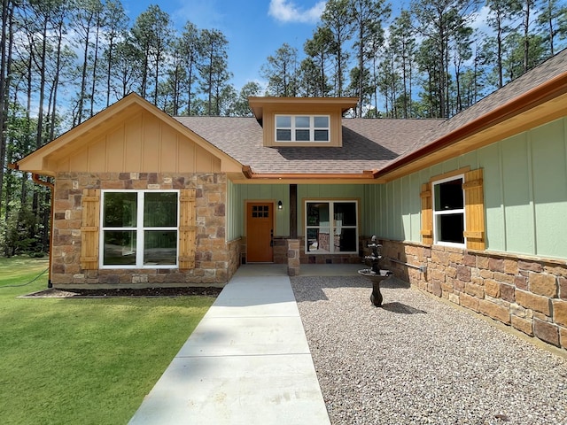 view of front facade featuring roof with shingles, board and batten siding, a front lawn, and stone siding