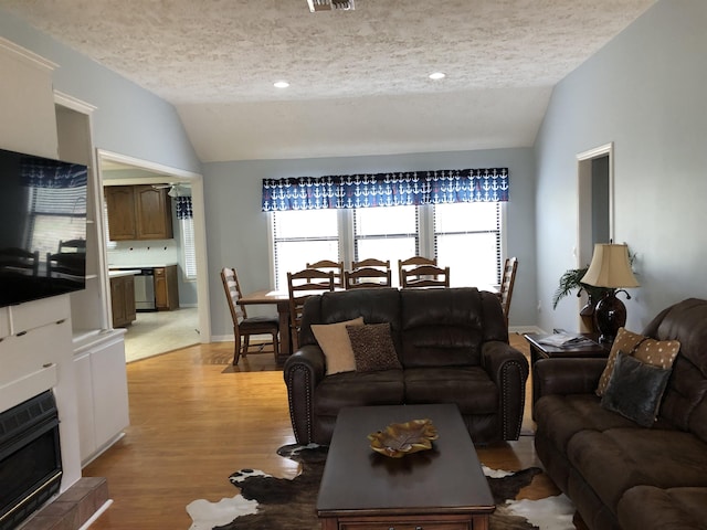 living room with vaulted ceiling, a tiled fireplace, and a textured ceiling