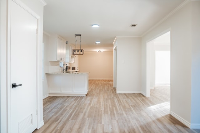 kitchen with light wood-type flooring, light stone counters, sink, white cabinets, and hanging light fixtures