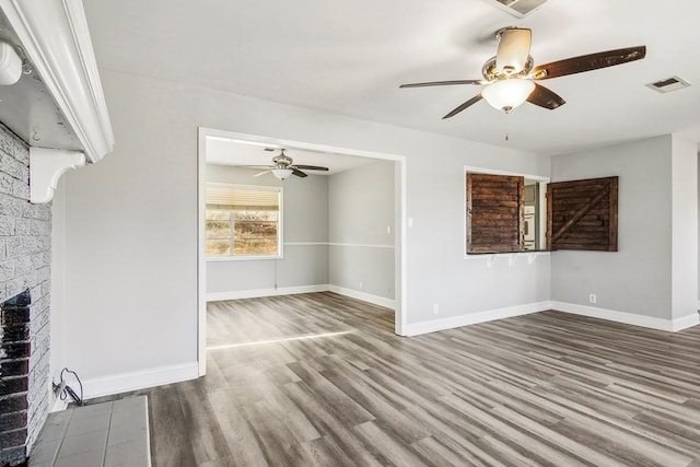 unfurnished living room with a brick fireplace, visible vents, baseboards, and wood finished floors