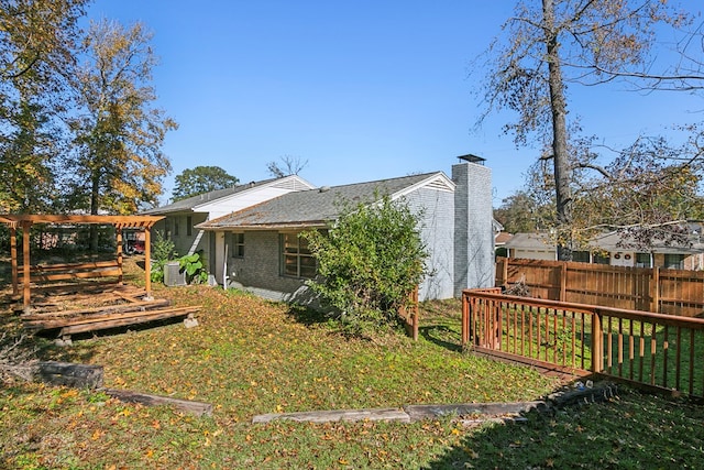 back of house featuring brick siding, a chimney, fence, and a lawn