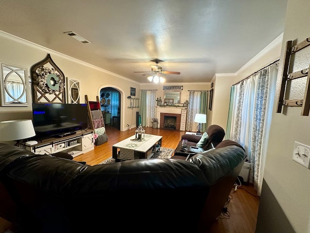 living room with hardwood / wood-style flooring, ceiling fan, ornamental molding, and a fireplace