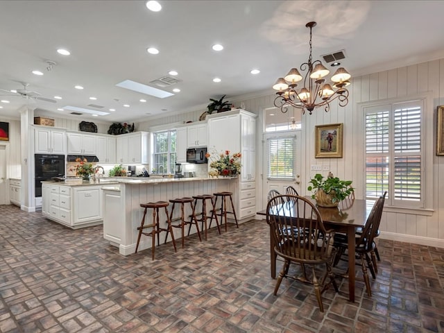 dining room with ceiling fan with notable chandelier, a skylight, crown molding, and sink