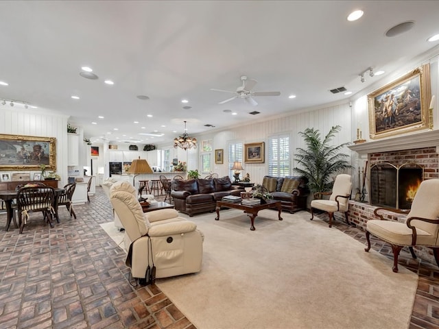 living room with crown molding, ceiling fan with notable chandelier, and a brick fireplace