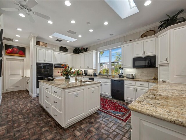 kitchen featuring a skylight, white cabinetry, sink, a kitchen island with sink, and black appliances