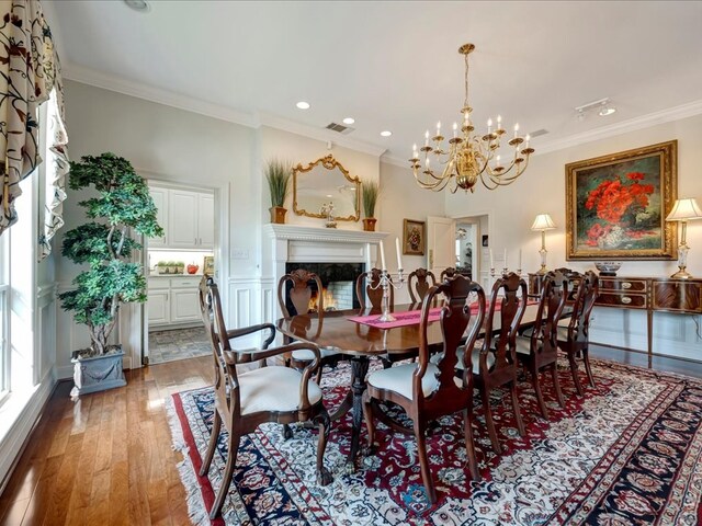 dining area with hardwood / wood-style floors, ornamental molding, a fireplace, and an inviting chandelier