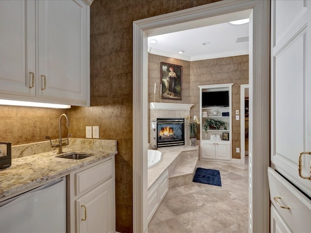 bathroom featuring a tub to relax in, crown molding, a tiled fireplace, vanity, and tile walls