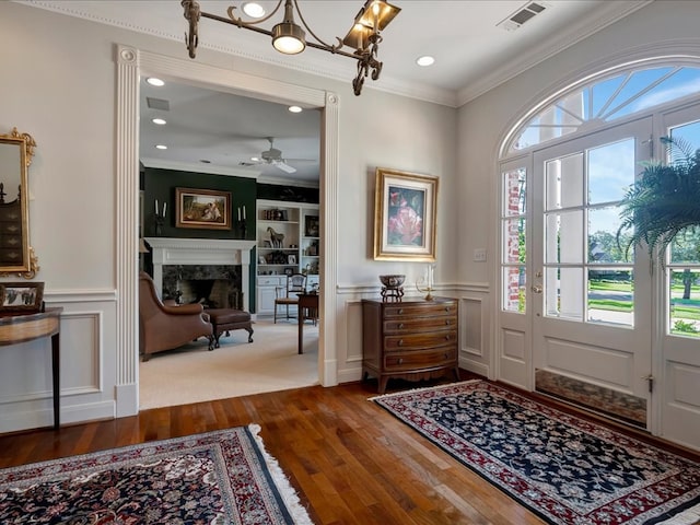 foyer entrance with hardwood / wood-style flooring, ceiling fan, ornamental molding, and a fireplace