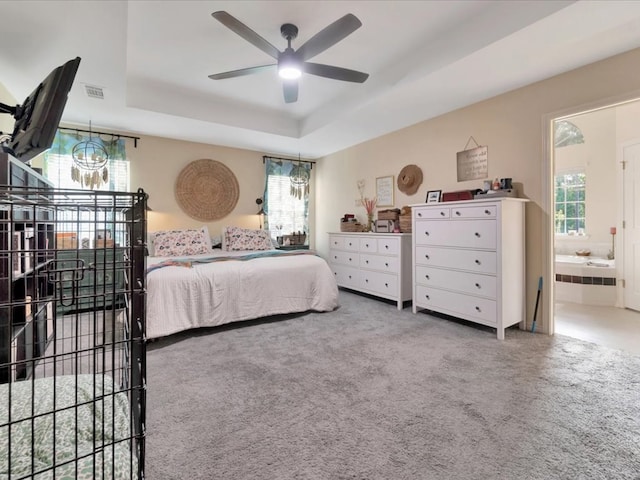 bedroom featuring a raised ceiling, ensuite bath, carpet floors, and ceiling fan with notable chandelier