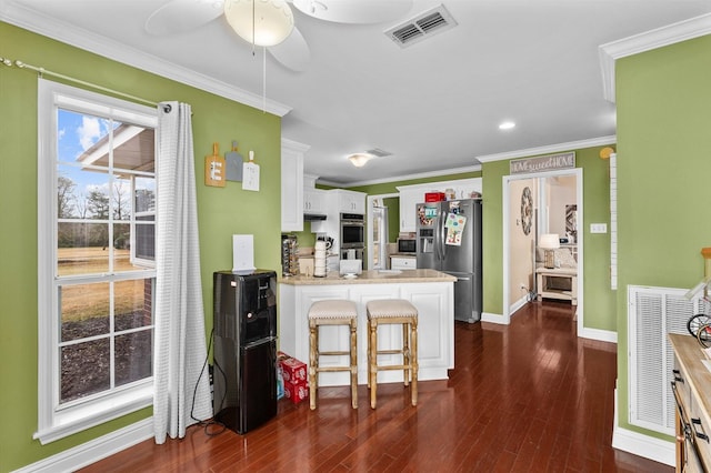 kitchen featuring appliances with stainless steel finishes, white cabinets, dark hardwood / wood-style flooring, a kitchen bar, and ornamental molding