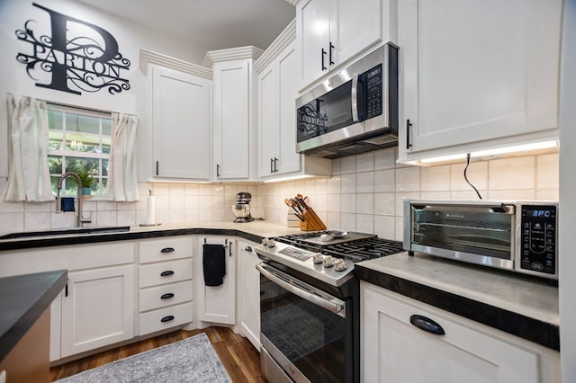 1208 Leslie Ln, Lufkin, TX 75901 - kitchen with stainless steel appliances, dark wood-style floors, white cabinetry, decorative backsplash, and dark countertops