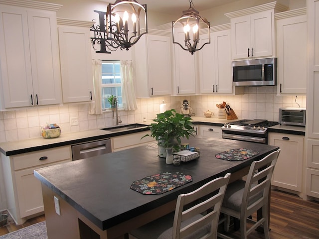 1208 Leslie Ln, Lufkin, TX 75901 - kitchen with stainless steel appliances, a chandelier, dark countertops, dark wood finished floors, and white cabinets