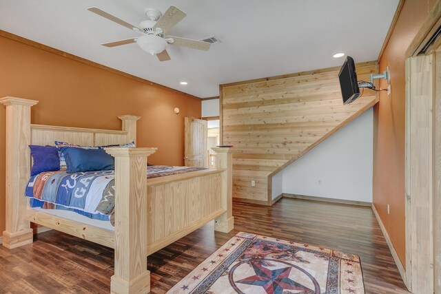 bedroom featuring ceiling fan, dark hardwood / wood-style flooring, ornamental molding, and wooden walls