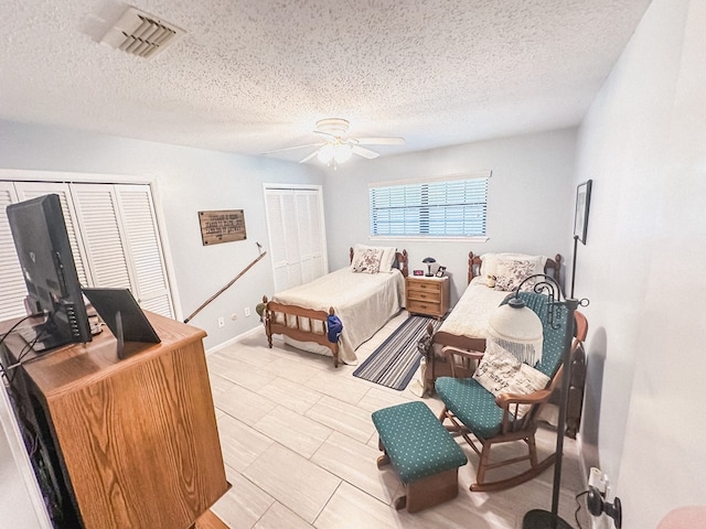 bedroom with two closets, ceiling fan, a textured ceiling, and visible vents