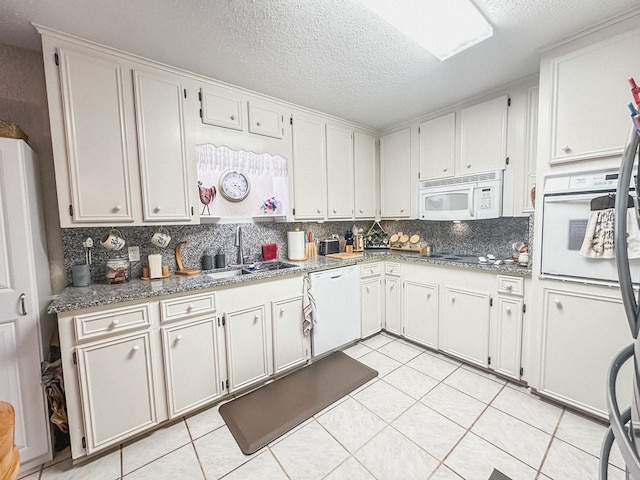 kitchen featuring backsplash, light tile patterned floors, a sink, white appliances, and a textured ceiling