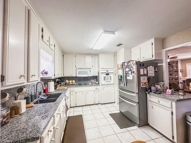 kitchen with a sink, a textured ceiling, visible vents, white appliances, and light tile patterned floors