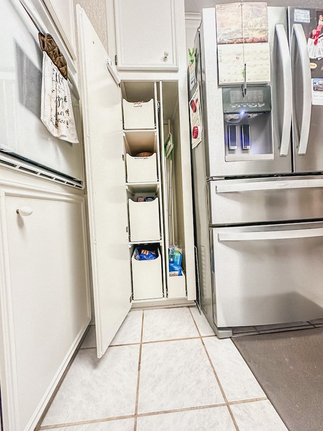 kitchen with stainless steel refrigerator with ice dispenser, light tile patterned flooring, and white cabinetry