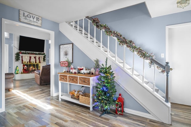 interior space featuring a warm lit fireplace, wood finished floors, and baseboards