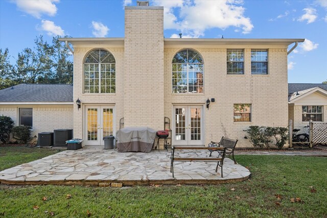 rear view of house with brick siding, a yard, french doors, a chimney, and a patio area