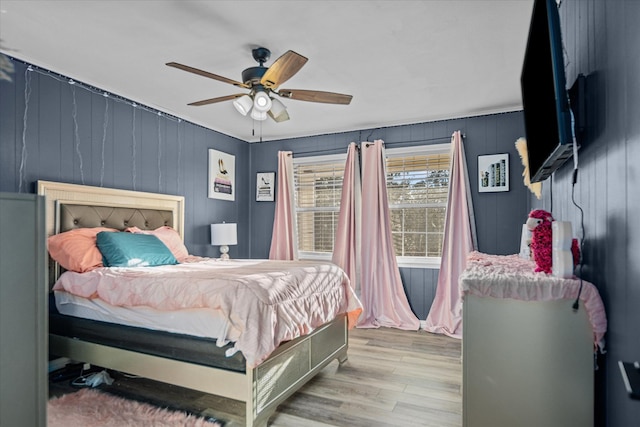 bedroom featuring light wood-type flooring, ceiling fan, and wooden walls