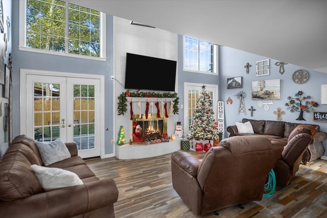 living room featuring hardwood / wood-style floors, a fireplace, a high ceiling, and french doors