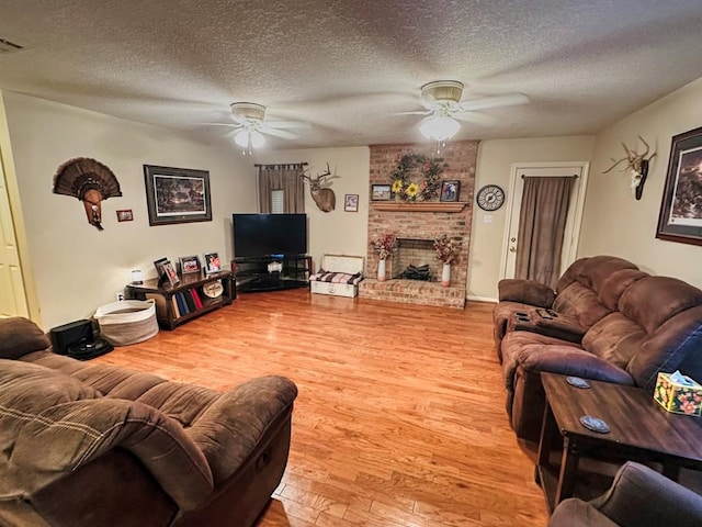 living room with a fireplace, ceiling fan, wood-type flooring, and a textured ceiling